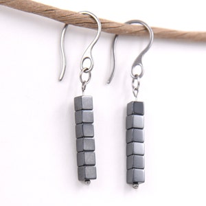 May include: A pair of silver earrings with a dangle design. Each earring features a row of seven small, gray, cube-shaped beads.
