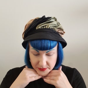 May include: A black, brown and green fabric hat with a ruffled design. The hat is being worn by a person with blue hair.