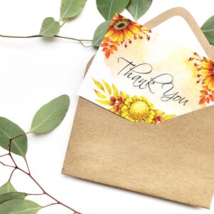 May include: A white card with a watercolor design of sunflowers and leaves in shades of yellow, orange, and red. The card has the text "Thank You" written in black calligraphy.