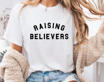 May include: White t-shirt with black text that reads "Raising Believers".