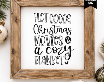 May include: A square wooden frame containing a white sign with black text that reads: HOT COCOA Christmas MOVIES & a cozy BLANKET. The frame has a natural wood grain finish and a rustic appearance, surrounding the printed message on a white background.