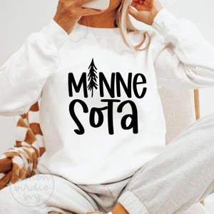 May include: White sweatshirt with the word "Minnesota" in black, with a tree graphic replacing the "I". The word "Sota" is below. The sweatshirt is a casual style.