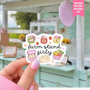Op de afbeelding: Een gestanste sticker met kleurrijke illustraties van een pot augurken, aardbeienjam, honing, een doos eieren, een brood en een mand met producten. De tekst "farm stand girly" staat in zwarte schrijfletters in het midden van de sticker.