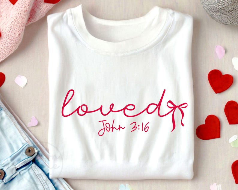 May include: White t-shirt with the word "loved" written in pink cursive script with a pink bow. The text "John 3:16" is written in pink below the word "loved".