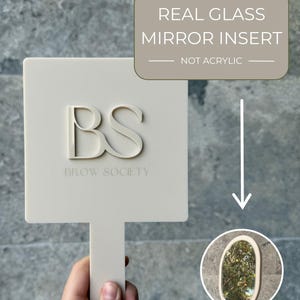 May include: A square beige handheld mirror with a handle, featuring the raised letters BS and the text BROW SOCIETY. A text box states REAL GLASS MIRROR INSERT NOT ACRYLIC, with an arrow pointing to a circular inset showing a real glass mirror.