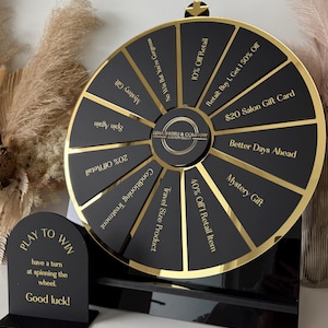 May include: A black and gold prize wheel featuring segments with text like "Mystery Gift" and "20% Off Retail." A sign says "Play to Win" with instructions. The wheel is for Lena Shkreli & Company.