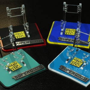 Può includere: Quattro espositori in acrilico trasparente con basi nere. Ogni espositore ha una base di colore diverso: rosso, blu, verde acqua e blu chiaro. Le basi hanno il testo "SUPER POCKET" e "HYPER MEGA TECH!" stampato su di esse.