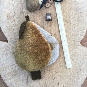 May include: A collection of sewing notions and tools arranged on a wooden surface. Includes a pear-shaped pincushion, black scissors, a thimble, a ruler, and various buttons. The pincushion is brown and tan, and the scissors have round handles.