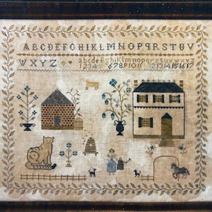 May include: A vintage needlepoint sampler with a brown wooden frame. The sampler features a white background with a brown and red brick house, a white house with black windows, a cat on a sled, a beehive, a flower pot, a tree, a fence, and a horse. The sampler also includes the alphabet and numbers.
