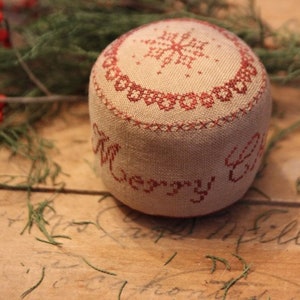 May include: A round, cream-colored fabric ornament with red embroidery. The ornament features a snowflake design and the words "Merry & Bright".