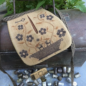 Può includere: Una piccola borsa di tessuto marrone e nero con una tracolla a scacchi neri e bianchi. La borsa ha un disegno floreale con fiori neri e un buco della serratura. La borsa è appoggiata su una scatola di metallo con una tracolla a scacchi neri e bianchi.