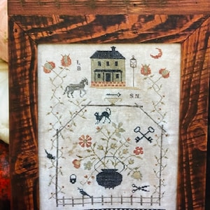 May include: A framed cross-stitch sampler with a black cat, a house, a key, a bird, and a cauldron. The sampler is titled "Blackwater Hollow 1759".