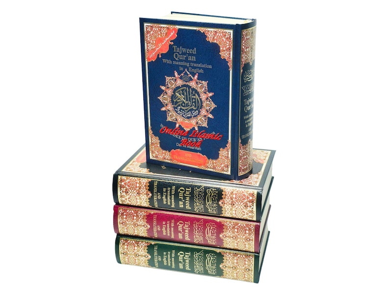 May include: A stack of four books with ornate covers. The top book is navy blue with gold accents and the title "Tajweed Qur'an" in English. The other books have burgundy, green, and black covers with similar gold detailing and text.