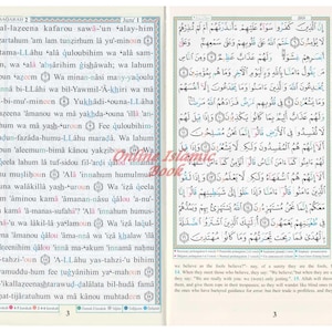 May include: Open book with Arabic text, featuring the Quran. The pages are cream-colored with black text, and the book is open to a double-page spread. The text is arranged in columns with a blue border. The book is on a white background.