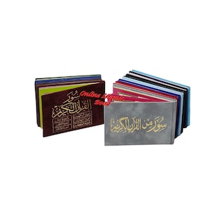 May include: Two stacks of small, colourful books. One stack is a dark burgundy colour with gold lettering. The other stack is a light grey colour with gold lettering. The books appear to be religious texts.