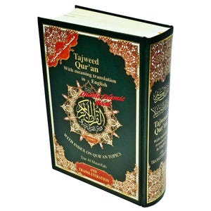 May include: A hardcover book titled "Tajweed Qur'an" with English translation. The cover is dark green with gold and red decorative elements. The book's spine also features text. The book is angled slightly, showcasing its cover and spine.