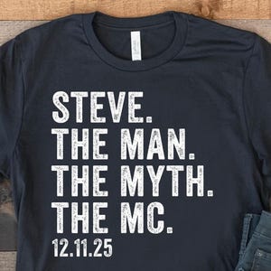 Peut inclure: Un t-shirt bleu marine avec le texte blanc "STEVE. THE MAN. THE MYTH. THE MC. 12.11.25." Le t-shirt est associé à un jean bleu et des baskets en toile blanches avec des accents rouges et bleus.