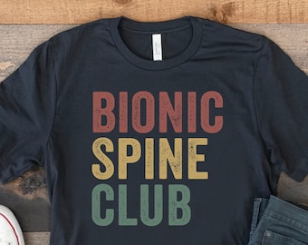 May include: A black t-shirt with a vintage-style graphic that reads "Bionic Spine Club" in red, yellow, and green text.