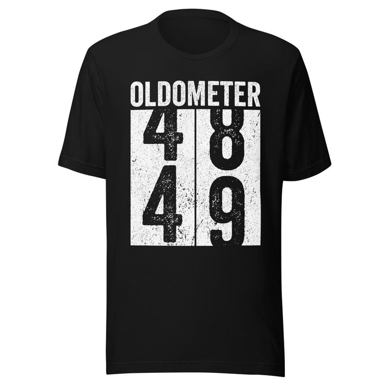 May include: Black t-shirt with the word "OLDOMETER" above the numbers 48 and 49 in a white, distressed font. The shirt is a crew neck and has short sleeves.