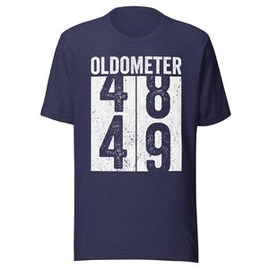 May include: Navy blue t-shirt with the word "OLDOMETER" above the numbers 48 and 49 in a white, distressed font. The shirt is a short-sleeved crew neck.