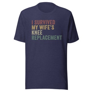 May include: Navy blue t-shirt with a vintage-style graphic that reads "I Survived My Wife's Knee Replacement".