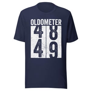 May include: Navy blue t-shirt with the word "OLDOMETER" printed in white. Below the word "OLDOMETER" are the numbers 48 and 49 in a white box. The shirt is a short-sleeved crew neck.