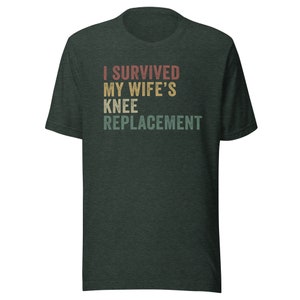 May include: A dark green t-shirt with the text "I survived my wife's knee replacement" in a vintage style font.