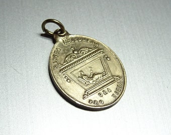 May include: A gold-colored metal pendant with a religious image and the inscription "SANCTA  RELIQUIA  PRO NOBIS ORA".