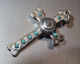 Puede incluir: Colgante de cruz de plata con piedras turquesa y una piedra transparente en el centro.