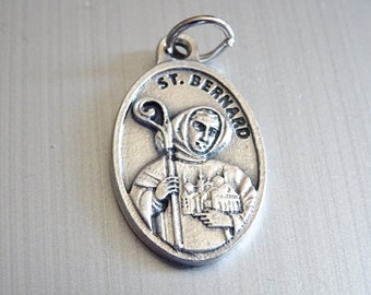 Può includere: Pendente ovale in argento con una raffigurazione di San Bernardo che tiene un bastone e una chiesa. Il pendente ha il testo "ST. BERNARD" inciso attorno al bordo.