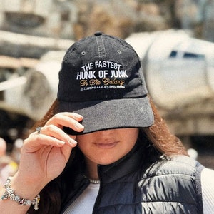 Könnte beinhalten: Eine schwarze Baseballkappe aus Cord mit dem Text "The Fastest Hunk of Junk in the Galaxy" in weißer und orangefarbener Stickerei. Der Text "Est. 1977 Galaxy, Far, Far Away" ist ebenfalls in weiß gestickt.