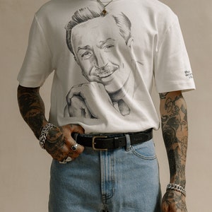 May include: A white t-shirt with a black and white illustration of Walt Disney on the front. The shirt has the text "the world studio" on the right sleeve.
