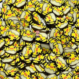 May include: A large group of yellow and white chick charms with black eyes and orange beaks. The charms are shaped like chicks hatching from eggs.