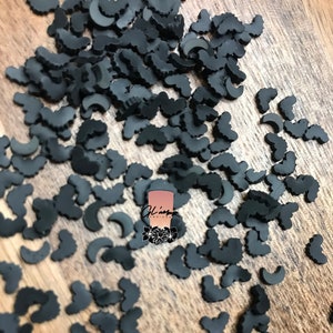 May include: A scattering of black, plastic, bat-shaped confetti. The confetti is on a wooden surface.