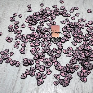 May include: A large quantity of pink alien head shaped resin charms. The charms are scattered on a light wood surface.