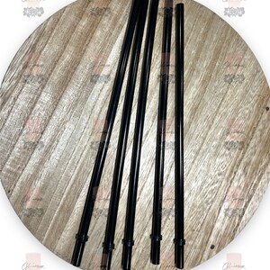 May include: Five black plastic drinking straws on a wooden surface.