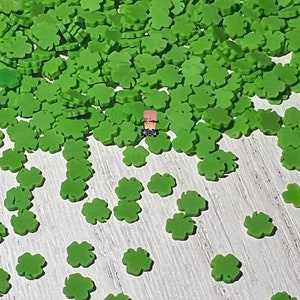May include: A large pile of green four-leaf clover confetti. The confetti is scattered on a white wooden surface.