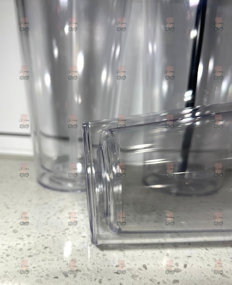 Puede incluir: Vasos de pl&aacute;stico transparente con base rectangular y cuerpo cil&iacute;ndrico. Los vasos son transparentes, lo que permite ver el contenido. Se ve una pajita negra en uno de los vasos. Los vasos est&aacute;n sobre una superficie blanca.