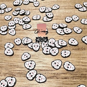 May include: A scattering of white and black Halloween themed stickers with a red and black design of a hockey mask. The stickers are on a wood surface.