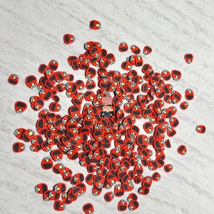 May include: A large quantity of red and black Elmo-themed confetti. The confetti is in the shape of Elmo's face with black eyes, a red nose, and a black mouth.