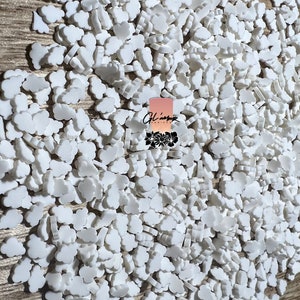 May include: A large quantity of white cloud-shaped sprinkles. The sprinkles are scattered on a wooden surface.