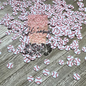 May include: A large pile of white and red baseball-themed confetti, scattered on a wood surface. The confetti is in the shape of baseballs with red stitching.