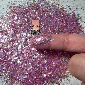 May include: Pink, white, and iridescent glitter with a variety of sizes. The glitter is shown in a pile on a white surface.