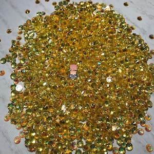 May include: A large pile of yellow iridescent rhinestones. The rhinestones are small and round, and they have a shiny, sparkly finish.