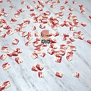 May include: A scattering of small, red and white, square-shaped, bacon-themed decorations on a white wooden surface.