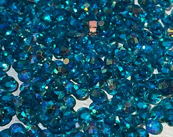 May include: A close-up shot of a pile of sparkling, teal-colored rhinestones. The gems are faceted, catching the light and creating a dazzling display. The rhinestones are scattered, suggesting a craft supply or decorative element.