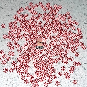 May include: A large quantity of red and white candy cane-shaped confetti. The confetti is scattered on a white surface with gray flecks.