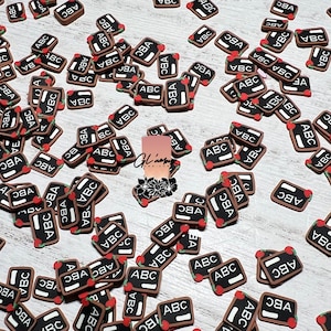 May include: A large quantity of small, brown, rectangular, chalkboard-style charms with the letters "ABC" written in white and a red apple design.
