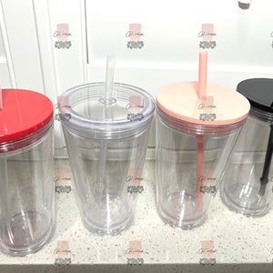 Puede incluir: Vasos de pl&aacute;stico transparente con tapas y pajitas de colores. Las tapas son rojas, rosa claro y negras. Las pajitas son transparentes, rosa claro y negras. Los vasos est&aacute;n sobre una superficie blanca.