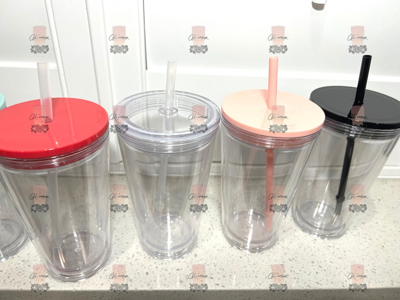 Puede incluir: Vasos de pl&aacute;stico transparente con tapas y pajitas de colores. Las tapas son rojas, rosa claro y negras. Las pajitas son transparentes, rosa claro y negras. Los vasos est&aacute;n sobre una superficie blanca.